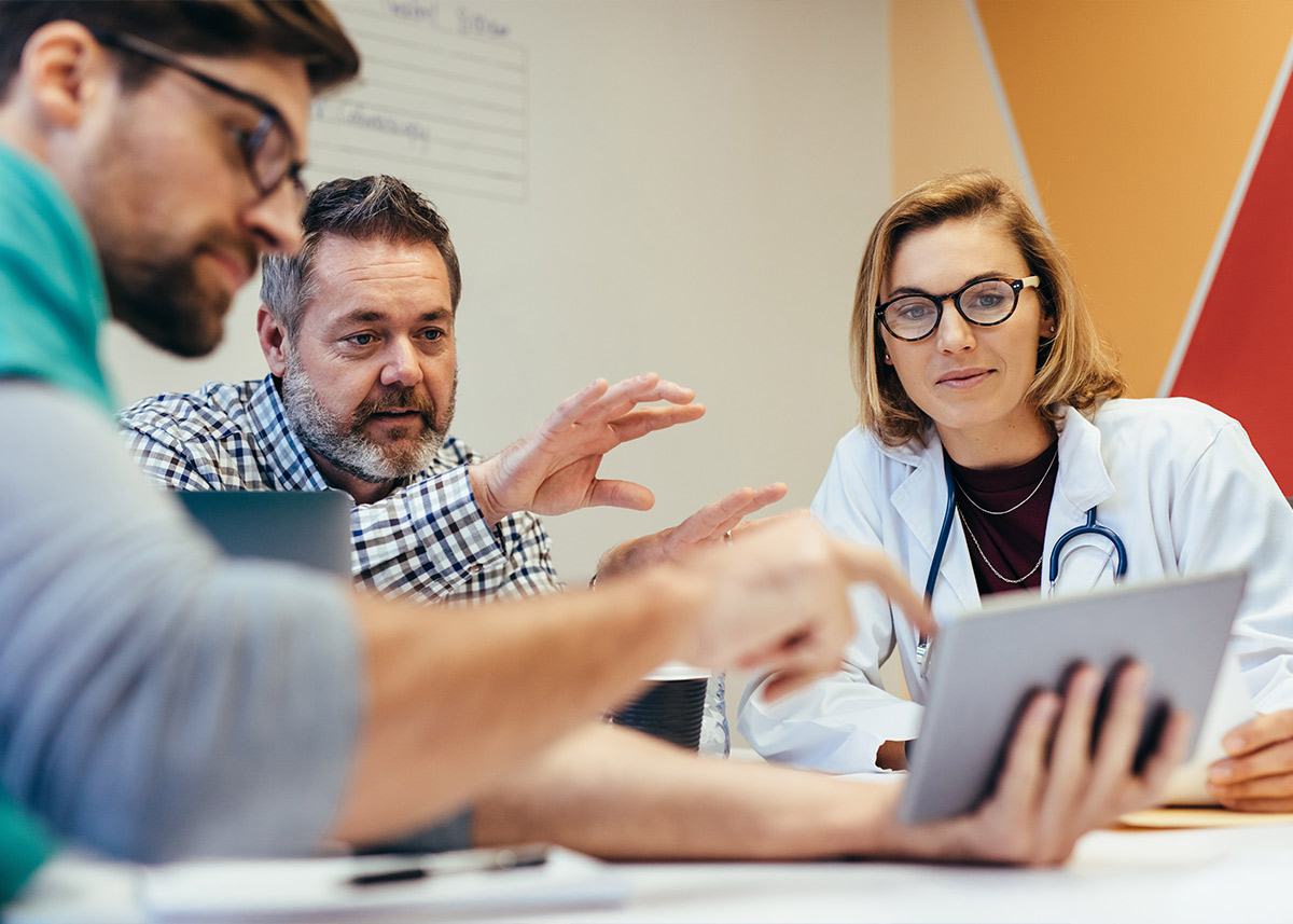 A doctor talks with colleagues about information on a tablet