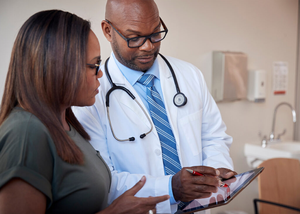 Healthcare professional wearing a white coat and stethoscope showing information to female patient.