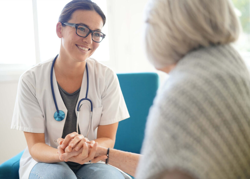 Medical professional holding the hand of an older female patient and smiling warmly at her.