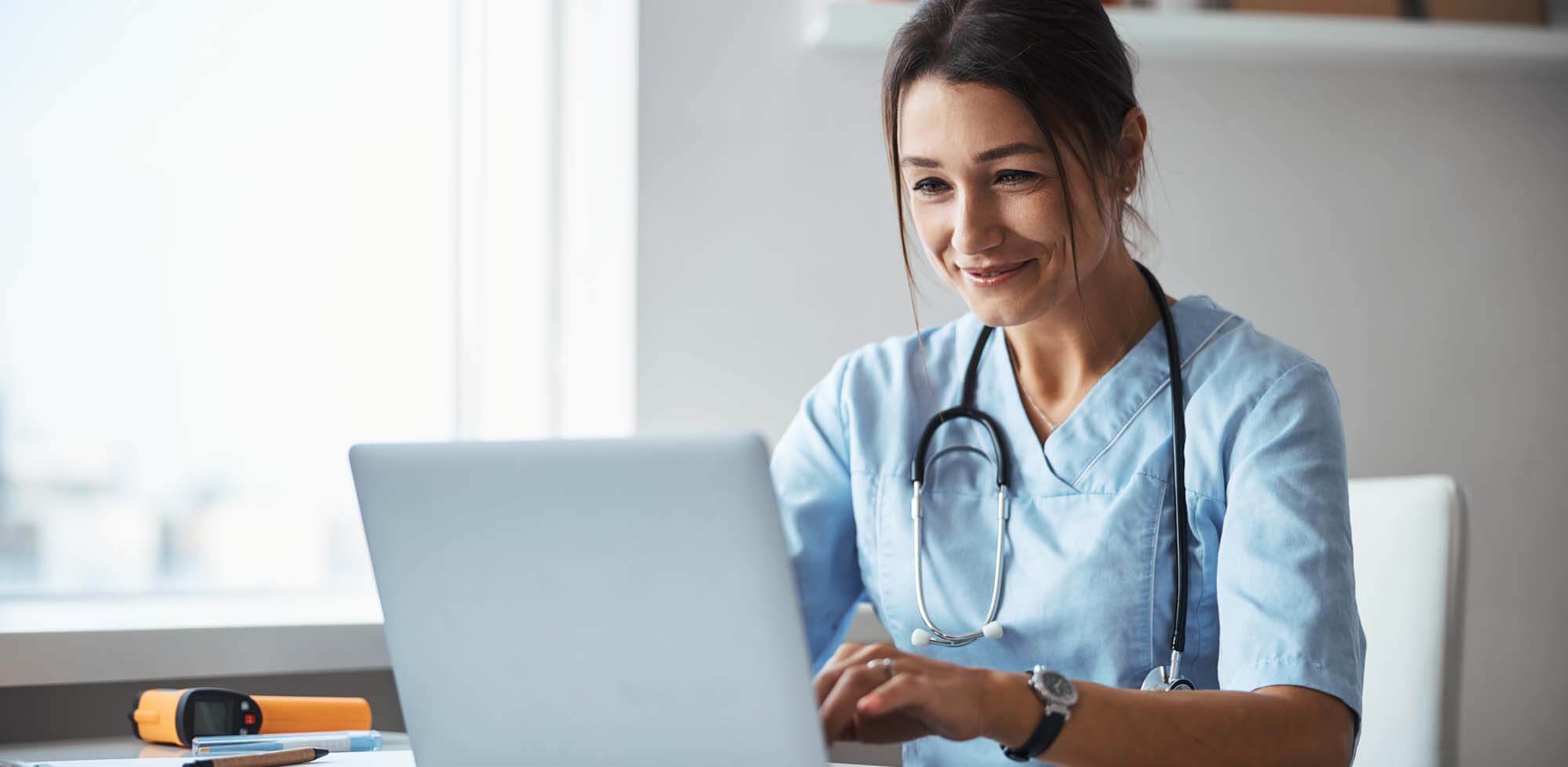 Female doctor wearing stethoscope works at her laptop.